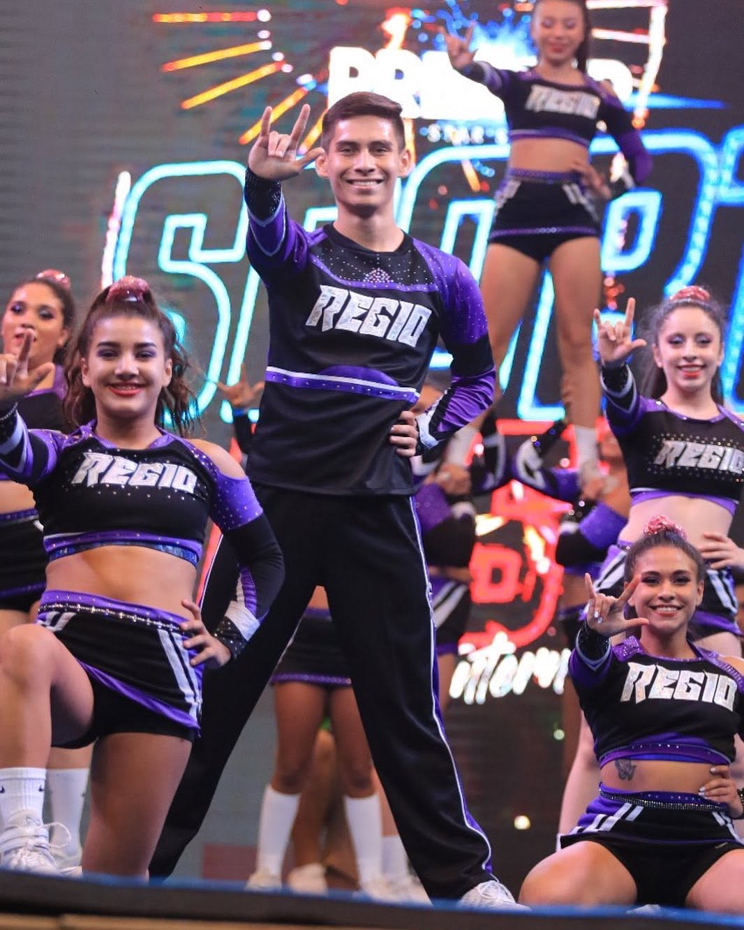 Atletas de Regio Cheer posando en el escenario con uniformes morados y negros